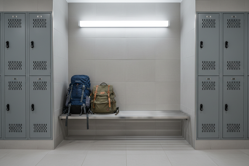 Locker room alcove with 48-inch wall-mounted bench between locker columns, backpacks on bench, clear tile floor beneath