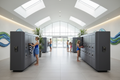 Modern aquatic center lobby with clusters of half-height phenolic day-use lockers, guests in swimwear, skylights above